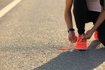 young sports woman runner tying shoelace on city road