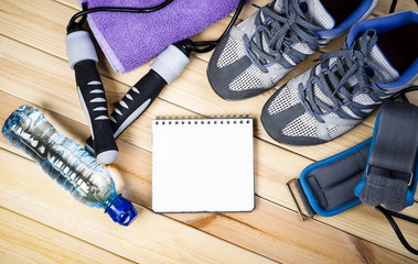 Jump Rope, Ankle Weights, Sport Shoes, Towel, Bottle Of Water And Notepad To Workout Plan On Wooden Floor. Sport Fitness Background