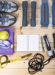 Sport Shoes, Dumbbells, Ankle Weights, Jump Rope, Towel, Tape Measure, Apple, Bottle Of Water, Notepad To Workout Plan On Wooden Floor. Sport Fitness Background