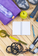 Sport Shoes, Dumbbells, Jump Rope, Towel, Tape Measure, Apple, Bottle Of Water, Notepad To Workout Plan On Wooden Floor. Sport Fitness Background