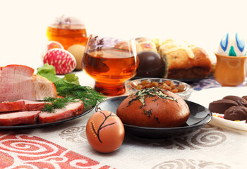 Traditional easter dinner set with sliced meat, bread with herbs, handmade colored eggs, chocolates, easter cake and glasses of juice on colorful tablecloth