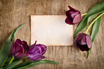 The old card and fresh tulips from two corners is lying on woode
