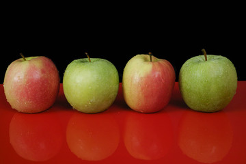 Fresh green and pink apples on red table top and black background