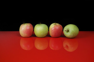 Fresh green and pink apples on red table top and black background
