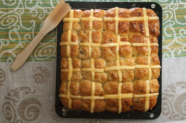 Top view of homemade easter hot cross buns on baking pan against colorful tablecloth