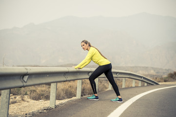 sport woman stretching leg muscle after running workout on asphalt road with dry desert landscape in hard fitness training session