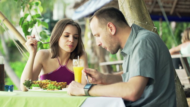 Attractive couple talking and eating lunch in restaurant with exotic garden
