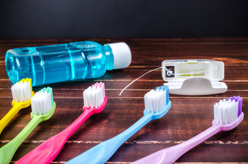 Set of colorful toothbrush with mouthwash and dental floss on wooden board