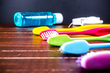 Set of colorful toothbrush with mouthwash and dental floss on wooden board