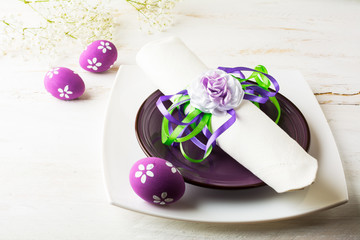 Obraz na płótnie Canvas Purple mauve lilac Easter table place setting with plate, napkin and purple Decorated Easter eggs on white wooden background