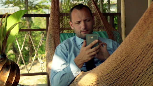 Young businessman using smartphone while lying on hammock 
