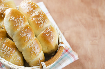 Fresh homemade bread rolls with sesam seed in basket on wooden t
