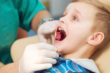 Dental inspection is being given to little boy surrounded by dentist and his assistant