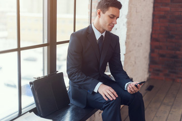 Businessman sitting waiting looking at mobile phone 