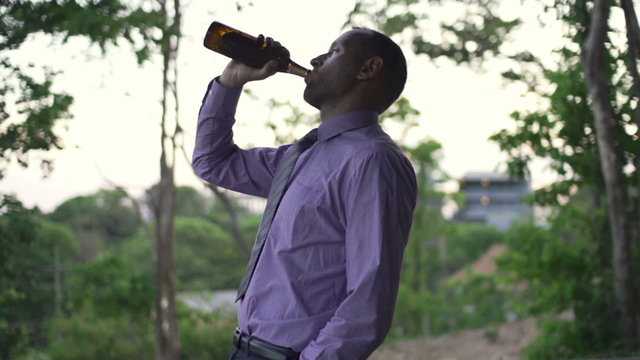 Young drunk businessman walking with beer on terrace in the evening
