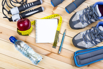 Sport Shoes, Dumbbells, Jump Rope, Ankle Weights, Tape Measure, Apple, Bottle Of Water, Notepad To Workout Plan On Wooden Floor. Sport Fitness Background