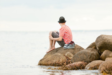 Trendy barefoot young man sitting on a rock