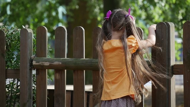 Girl is Climbing to The Wooden Fence Girl's Back Slow Motion Little Girl With Long Fair Hairs in Orange T-Shirt is Playing Outdoors at the Playground