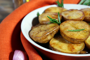 Delicious baked potato with rosemary in bowl on table close up