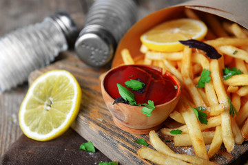 French fried potatoes in craft paper on cutting board