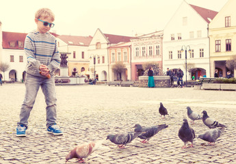 Boy feeding doves on the old city square