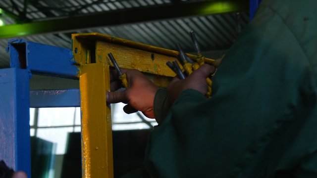 Two Workers in Uniform Are Untwisting The Bolts in Metal Frame, Smooth Glass Sheet is in the Frame,Before the Test,Factory Logo on the Worker's Jacket
