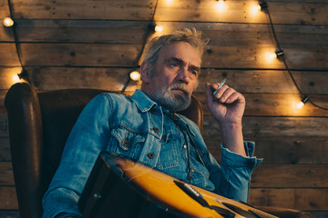 Smoking senior guitarist with beard sitting in chair in front of