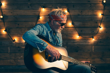 Senior guitarist with beard sitting on chair playing guitar in f