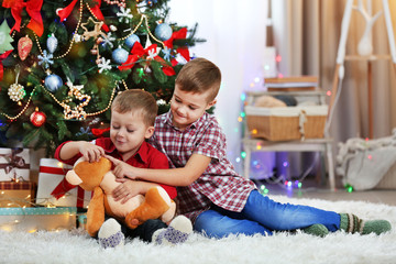 Two cute small brothers with teddy bear on Christmas tree background