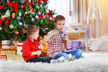 Fototapeta na wymiar Two cute small brothers blows soap bubbles on Christmas tree background