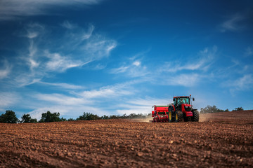 Naklejka premium Farmer with tractor seeding crops at field