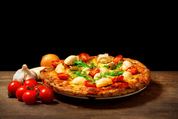 Delicious pizza and fresh vegetables on wooden table against black background, close up