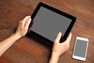 Mobile phone and female hands using tablet, on the wooden background