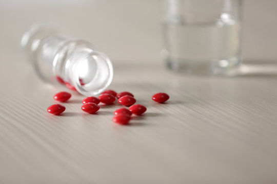 Red capsules spilled from pill bottle and glass of water on the table, close up