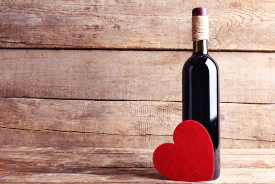 Red felt heart with wine bottle on wooden background