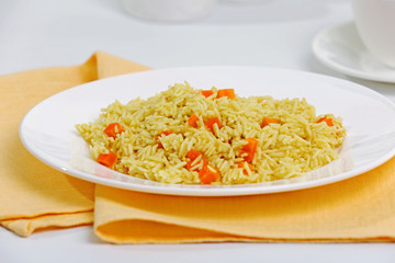 Stewed rice with a carrot on a white plate, close up