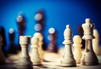 Chess pieces and game board on blue blurred background