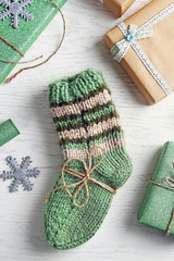 Pair of knitted socks with wrapped gifts for Christmas on light table