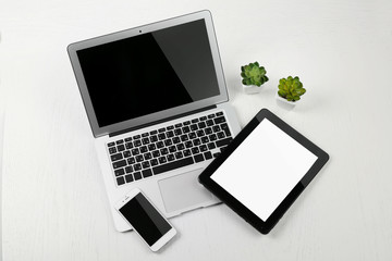 Different modern devices with green plants on light table