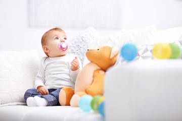 Sweet baby girl with a soother sitting on a sofa