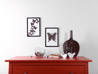 Room interior with red wooden commode, vase and frames on light wall background