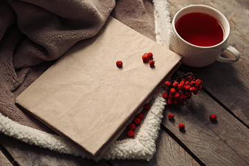 A book, a cup of tea, rowan berries and a blanket on the floor, close-up