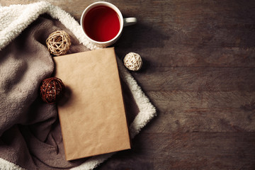 A book, a cup of tea, decorative balls and a blanket on the wooden background