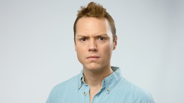 Young adult man looks at camera serious with a surprise expression in the face. He tries to see or understand something.