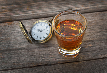 Faceted glass of whiskey and Vintage pocket watch on wooden text