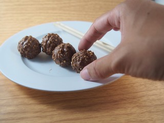 Pinking hand milk chocolate balls with almond and peanuts on white dish