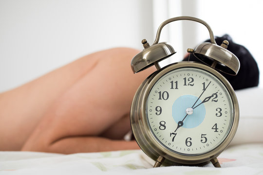 Alarm clock with man waking up on bed in background (Shallow depth of field)