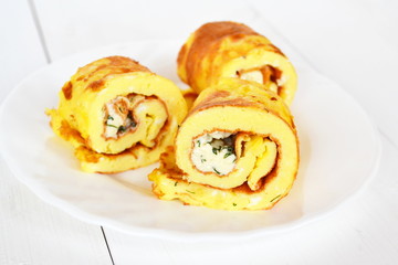 Rolls of omelette with cheese on a plate on white wooden background