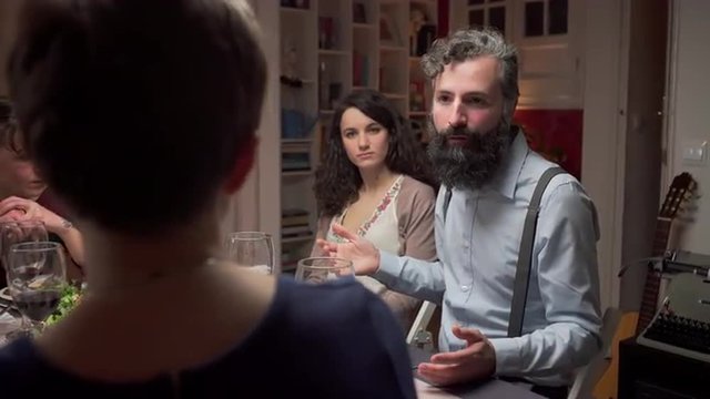 Young adult hipster man in a dinner with friends. He is talking. The camera moves. 4K, UHD