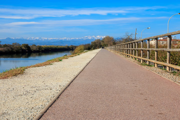 Deserted gravel hiking path among ambient greenery near river with snowy mountains peaks in background